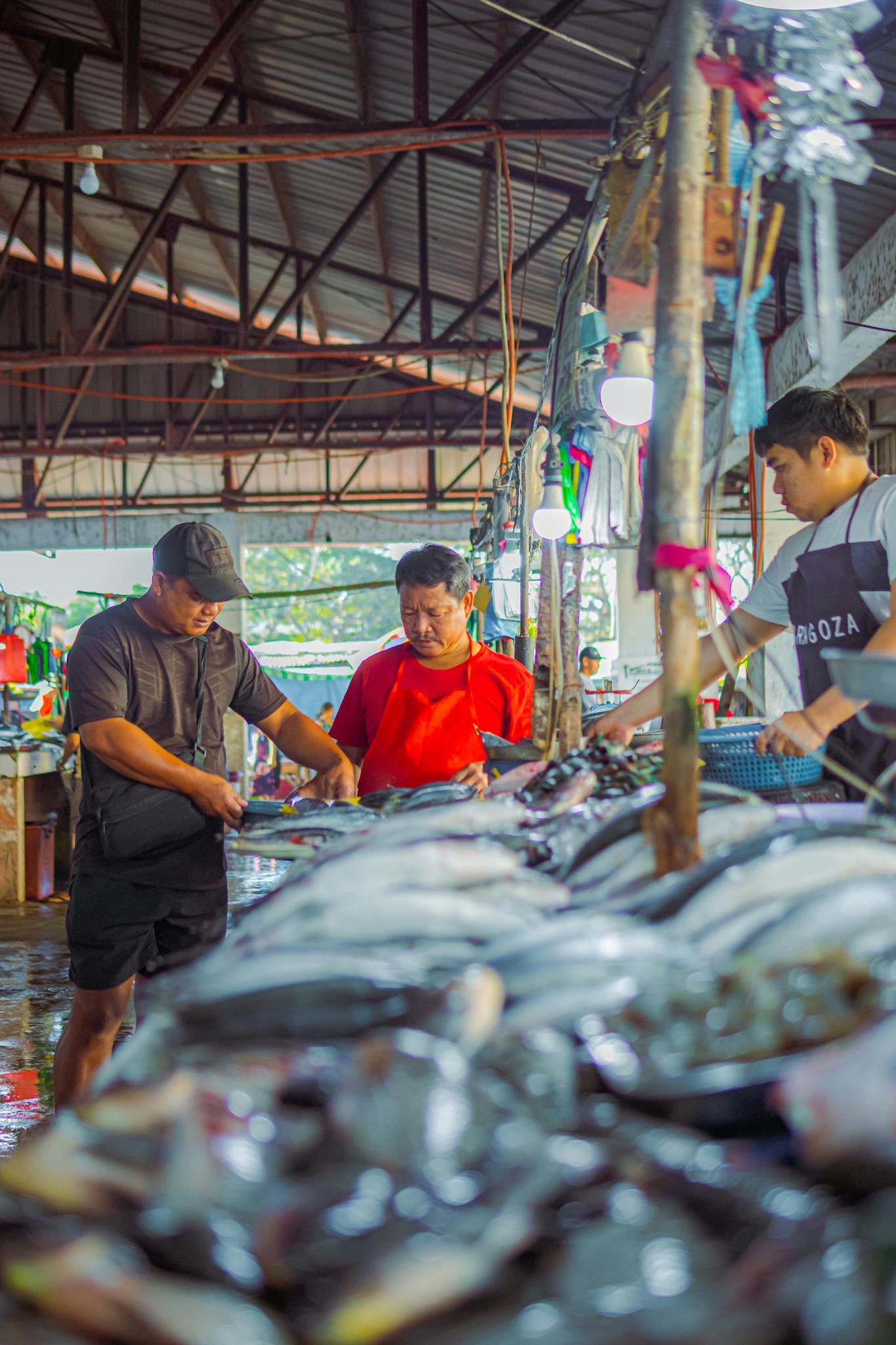 Three men buying seafood at a bustling market stall with fresh fish on display.